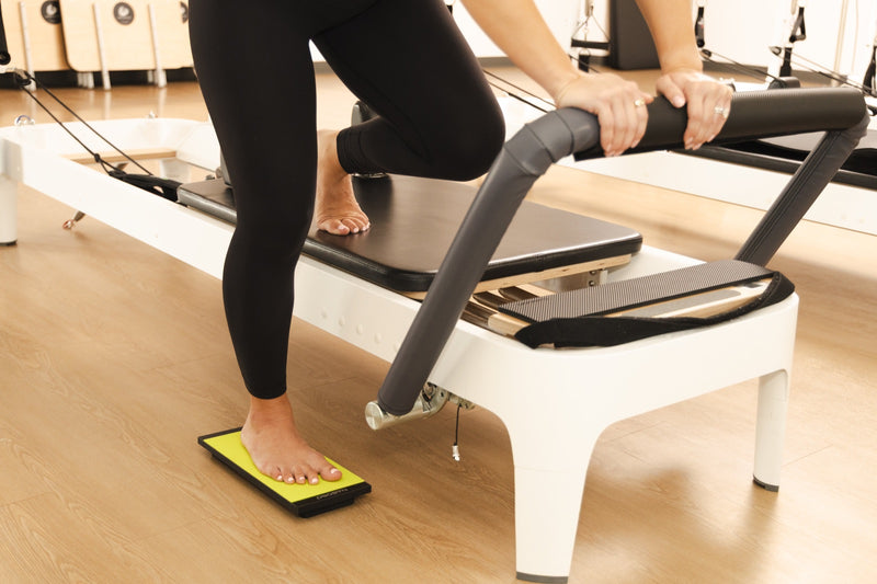 A standing lunge beside the reformer with the front foot on the Kinesis Board